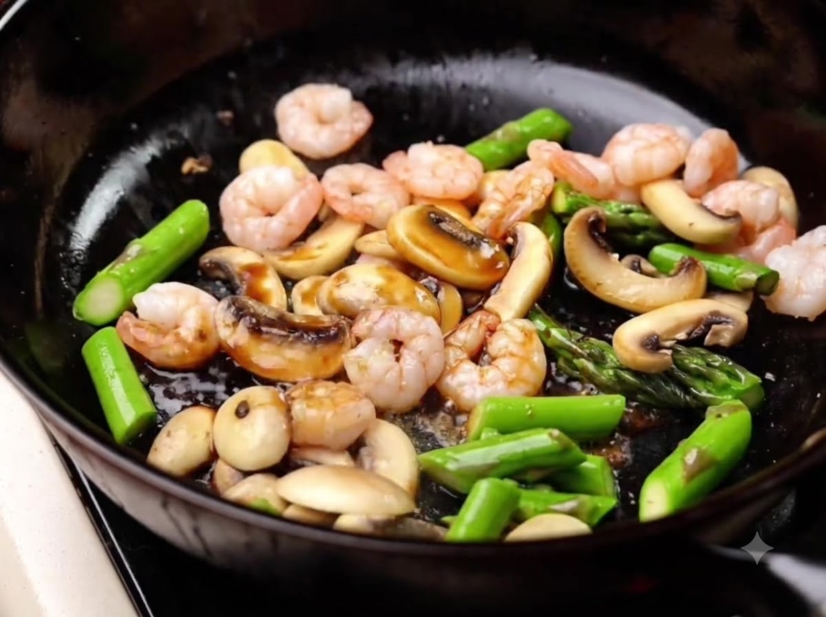 Sauce soja claire versée dans la poêle sur les crevettes, les asperges et les champignons, puis mélangée.
