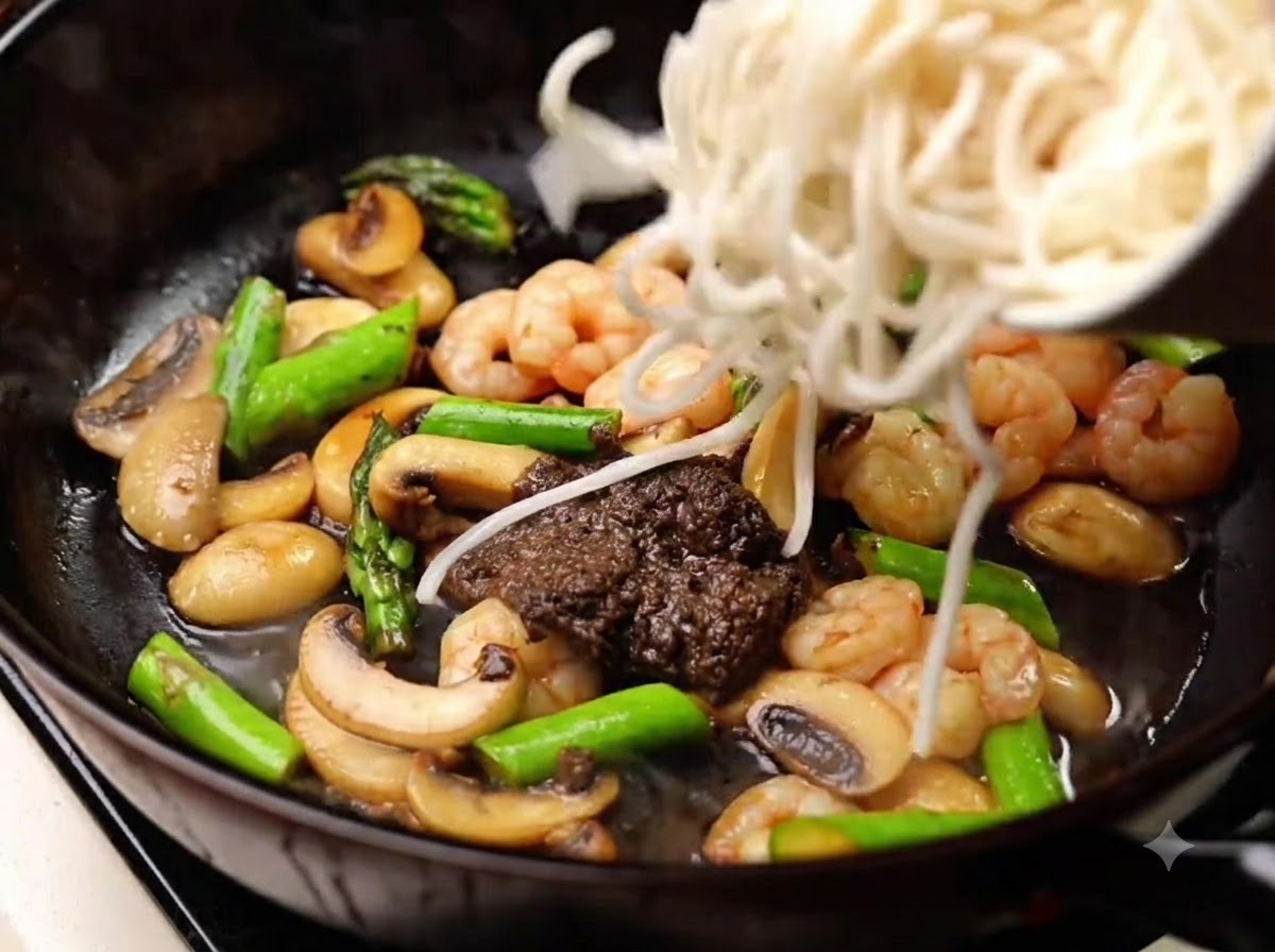Nouilles cuites ajoutées dans la poêle pour être mélangées avec la sauce, les champignons, les crevettes et les asperges.