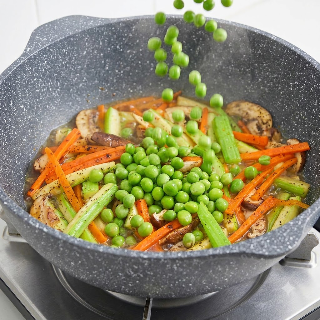 Des petits pois tombant du dessus dans une poêle remplie de champignons tranchés, de carottes et de courgettes.