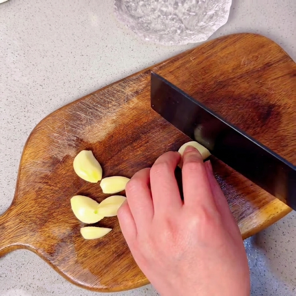 Gousses dail disposées sur une planche à découper en bois prêtes à être émincées.