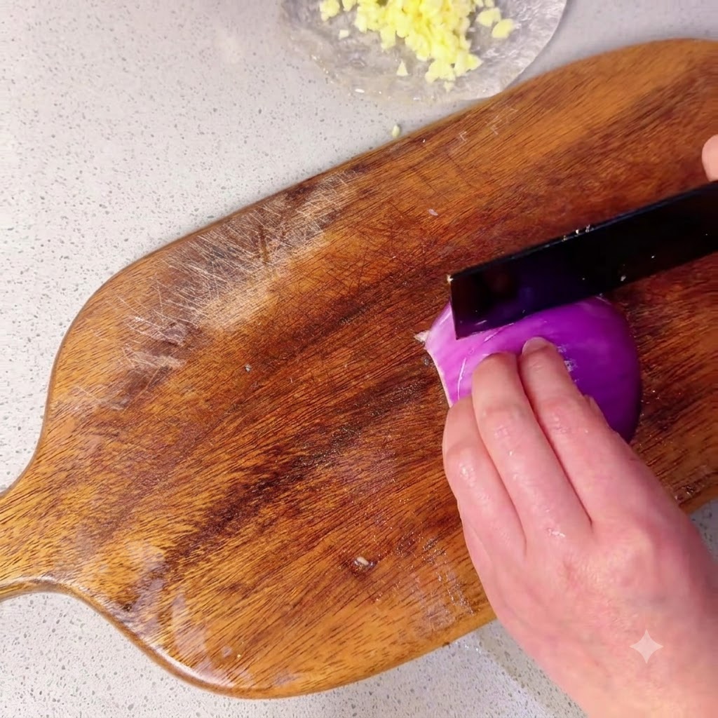 Moitié dun oignon rouge en cours de découpe en petits morceaux sur une planche à découper en bois.