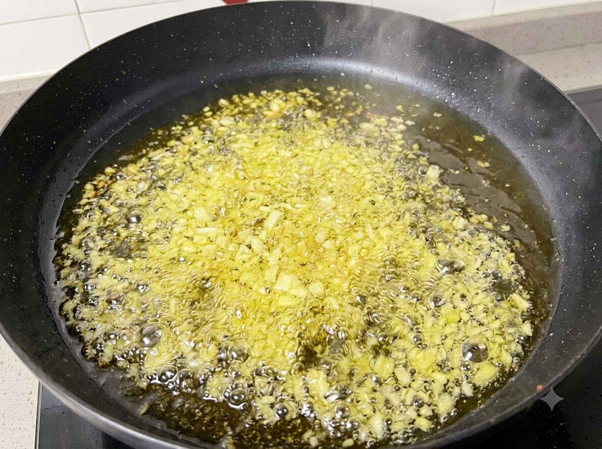 Ail émincé et oignons en train de frire et de bouillonner dans de lhuile chaude à lintérieur dune poêle noire.