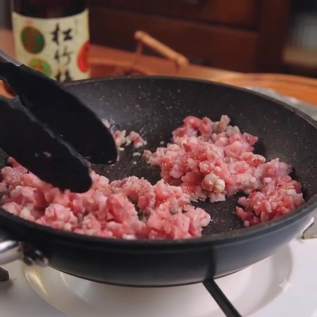 Porc haché cru et ail mélangés dans une poêle noire à laide de pinces de cuisine.