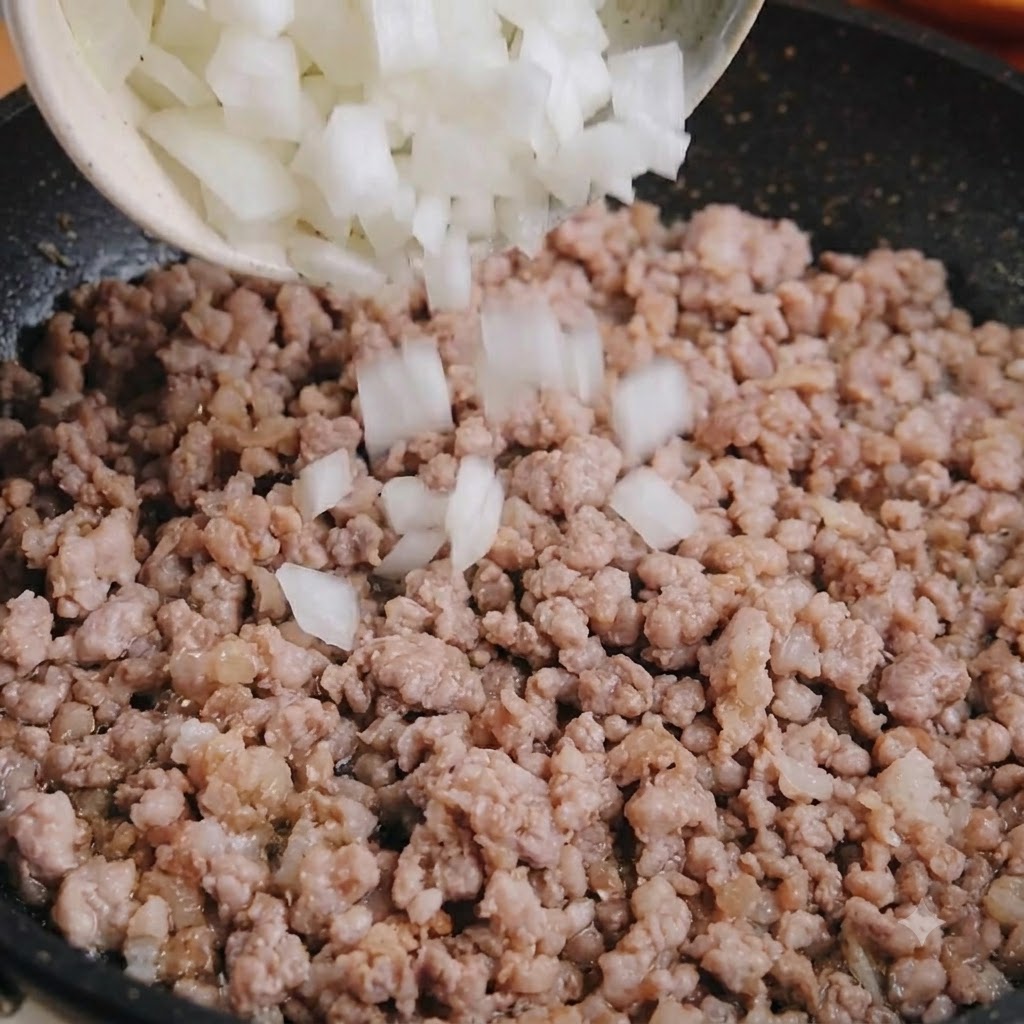 Oignon blanc en dés versé dun bol dans une poêle de porc haché cuit.