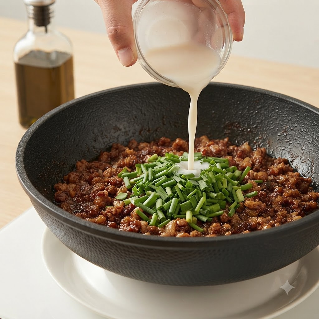 Main versant un mélange de fécule blanche dun petit bol en verre dans une poêle de viande hachée et de ciboulette.