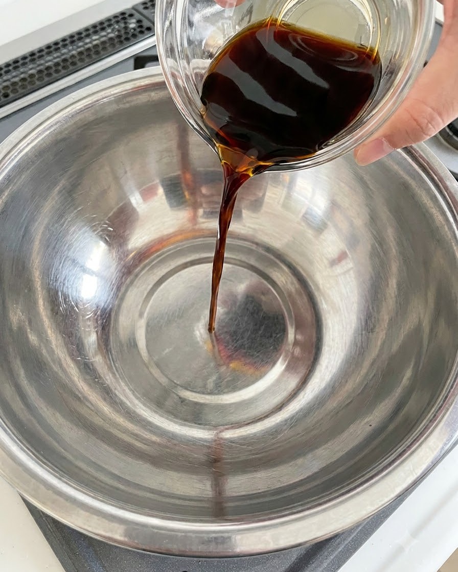 Sauce soja noire versée dun récipient en verre dans un bol en acier inoxydable.