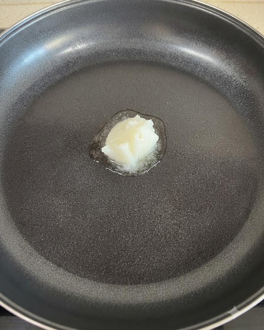 Une noisette de saindoux blanc fondant au centre dune poêle antiadhésive.