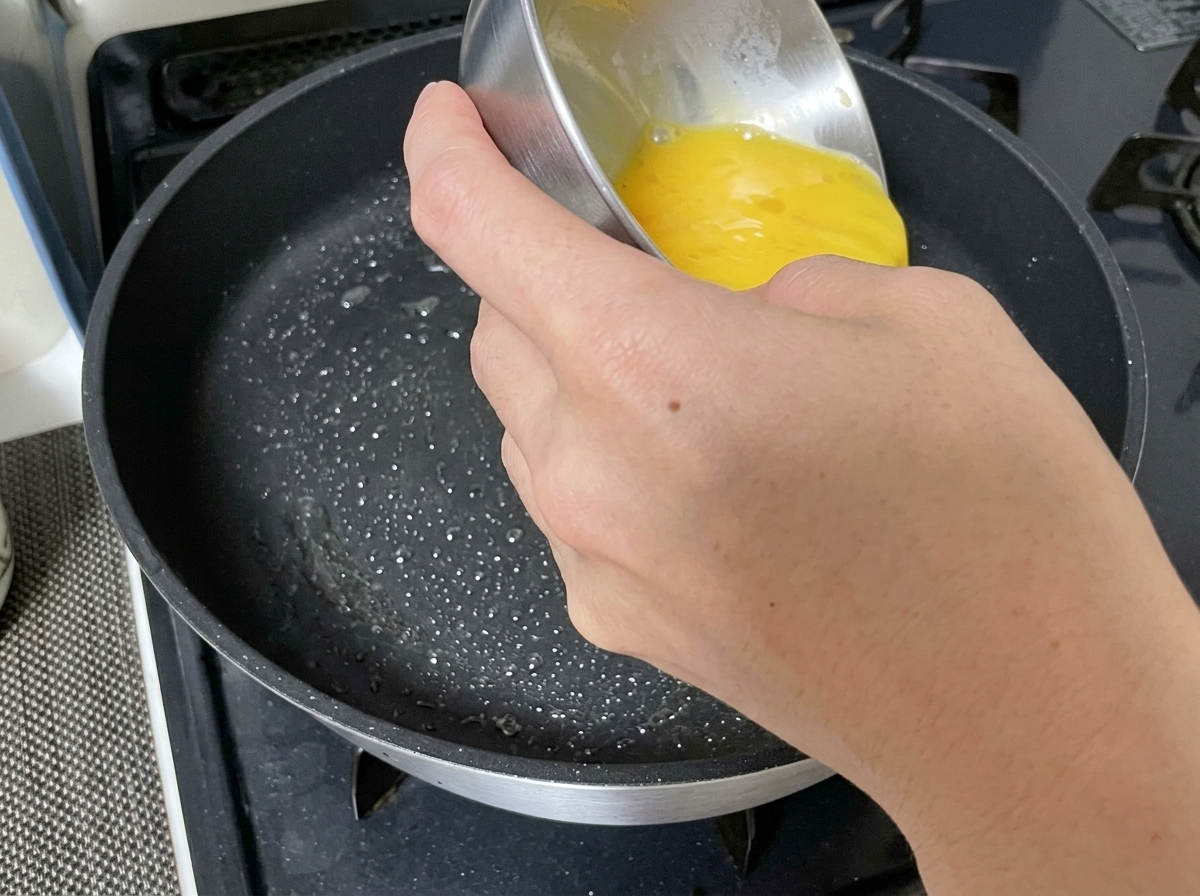 Œuf battu versé dans une poêle huilée.