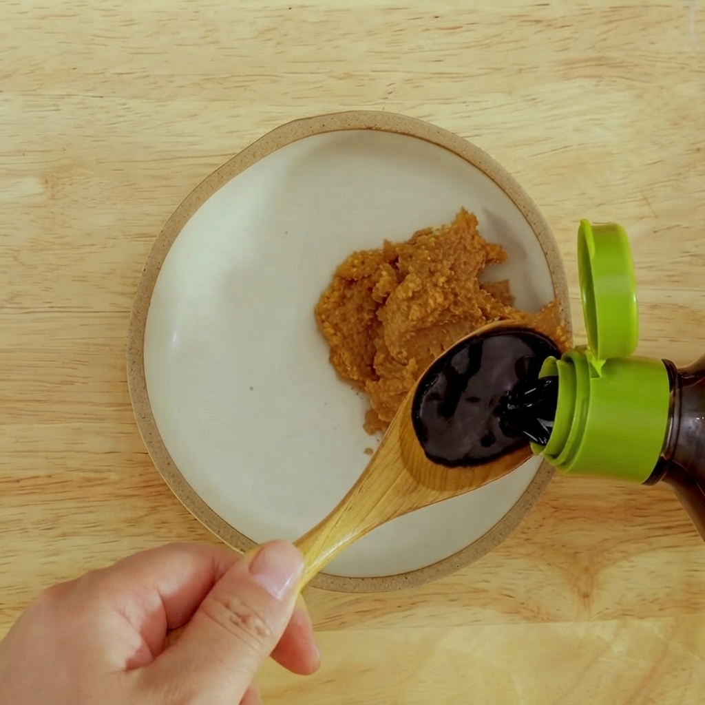 De la sauce soja foncée versée dans un bol contenant de la pâte de miso rouge épaisse.