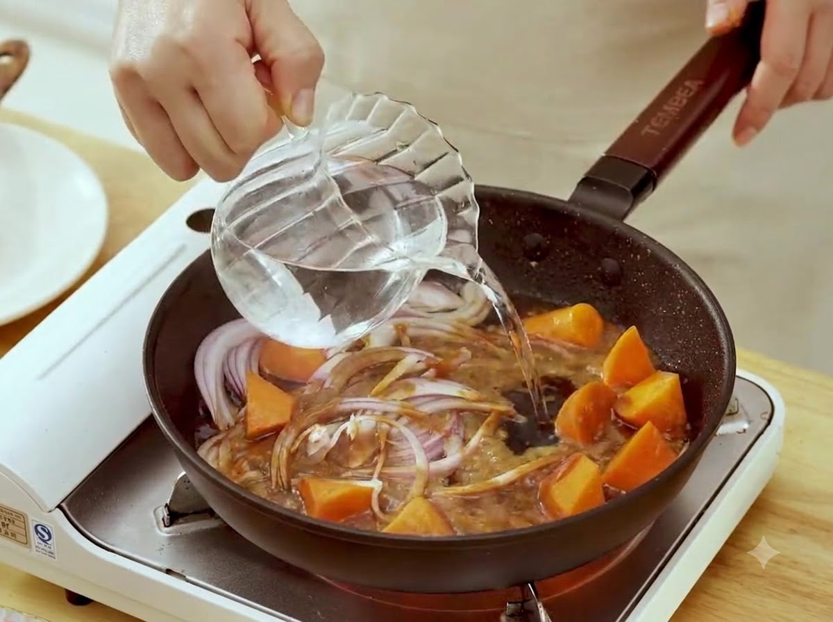 De leau versée dune pichet en verre dans une poêle avec des oignons rouges émincés et des morceaux de carotte dans la sauce miso.