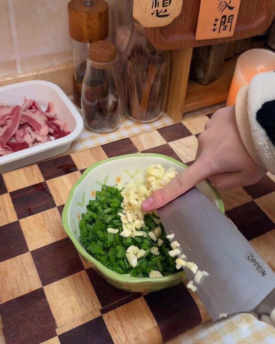 De lail finement haché ajouté dans un bol contenant des oignons nouveaux hachés et des épices.