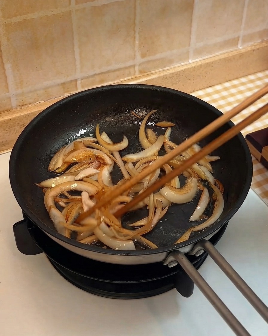Des lanières doignon sautées dans une poêle à laide de baguettes en bois.