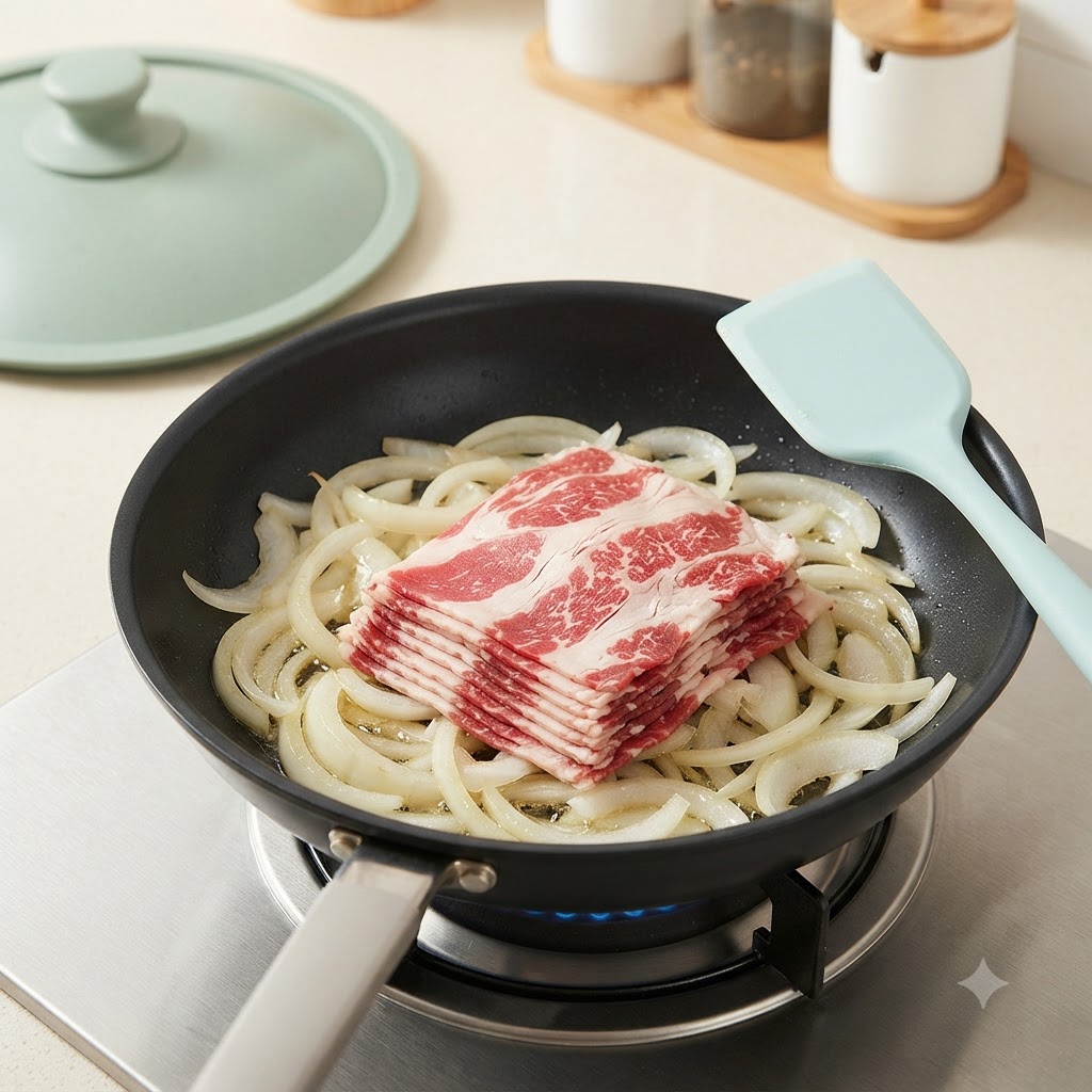 Morceaux de bœuf émincés déposés sur les oignons sautés dans une poêle sur la cuisinière.
