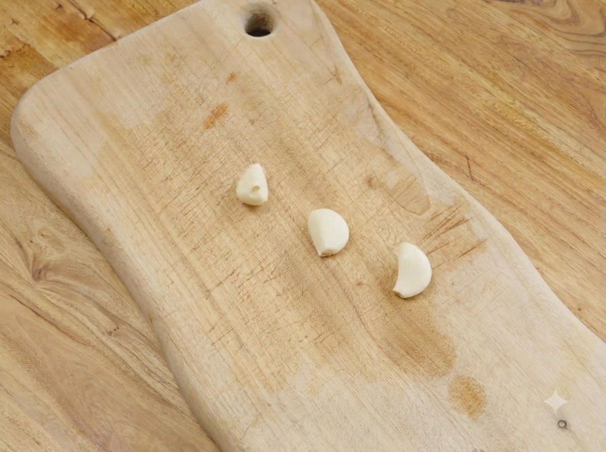 Trois gousses dail pelées reposant sur une planche à découper en bois.