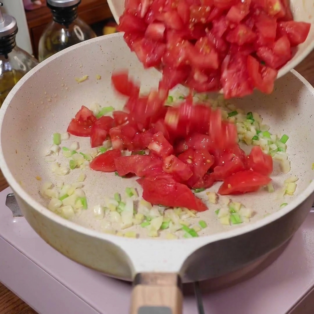 Tomates en dés versées dans une poêle avec les aromates revenus.