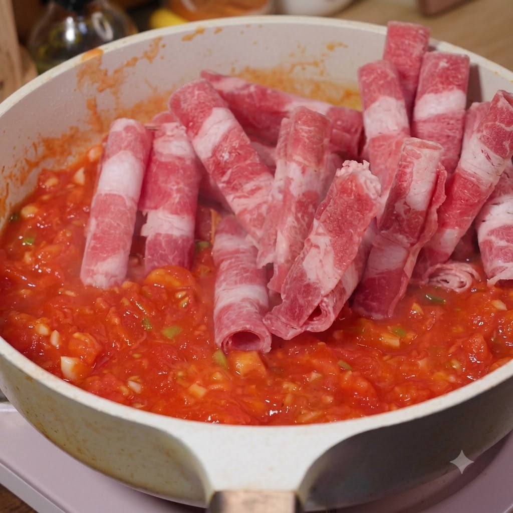 Tranches de bœuf gras ajoutées dans une poêle avec les tomates en train de rissoler.