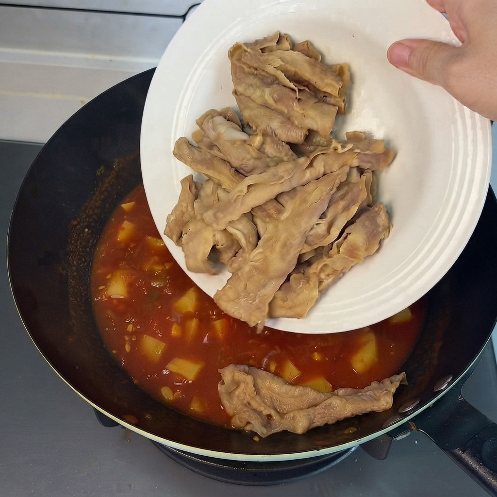 Rouleaux de bœuf pré-blanchis glissant dune assiette blanche dans le bouillon rouge savoureux du wok.