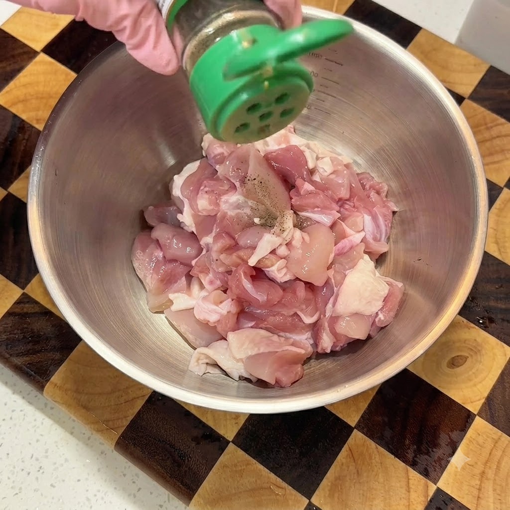Saupoudrage de poivre noir à partir dun shaker vert sur du poulet cru coupé en dés dans un bol mélangeur en métal.