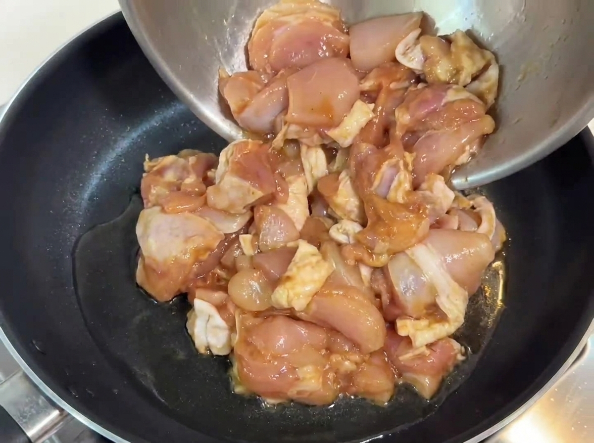Morceaux de poulet marinés versés dans une poêle avec de lhuile chaude.