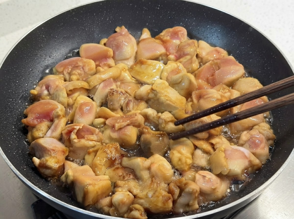 Morceaux de poulet marinés sautés dans une poêle et retournés délicatement à laide de baguettes en bois.