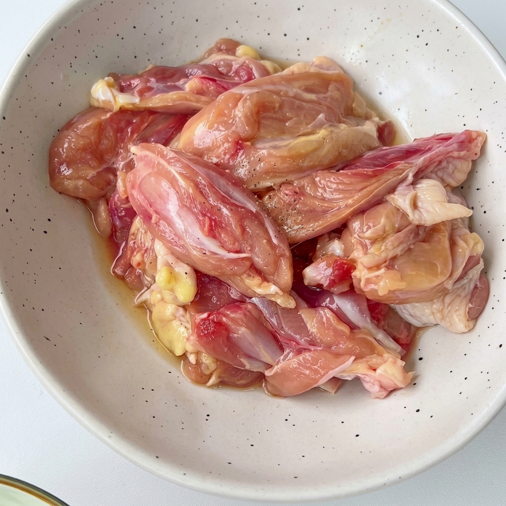 Morceaux de poulet coupés dans un bol blanc moucheté, mélangés avec des assaisonnements et des aromates.