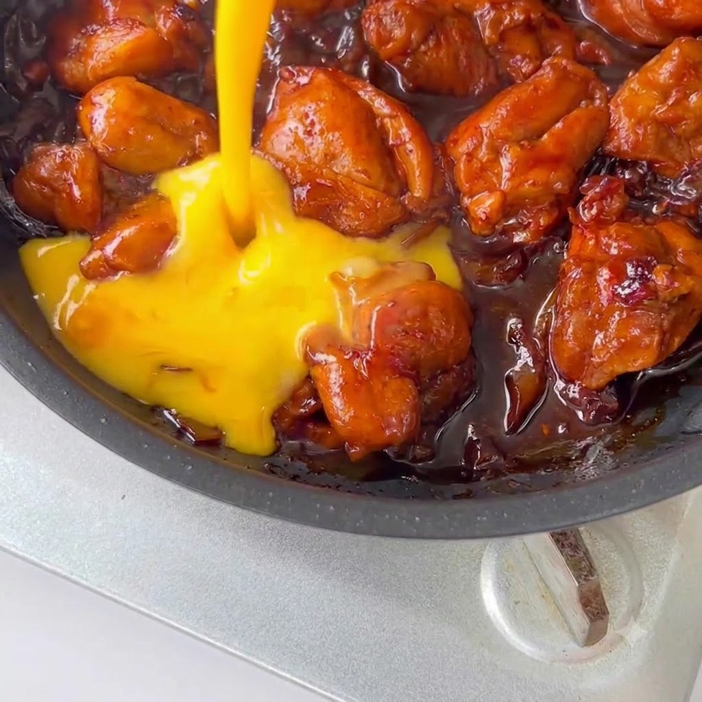 Œufs battus versés sur le poulet et la sauce dans une poêle.