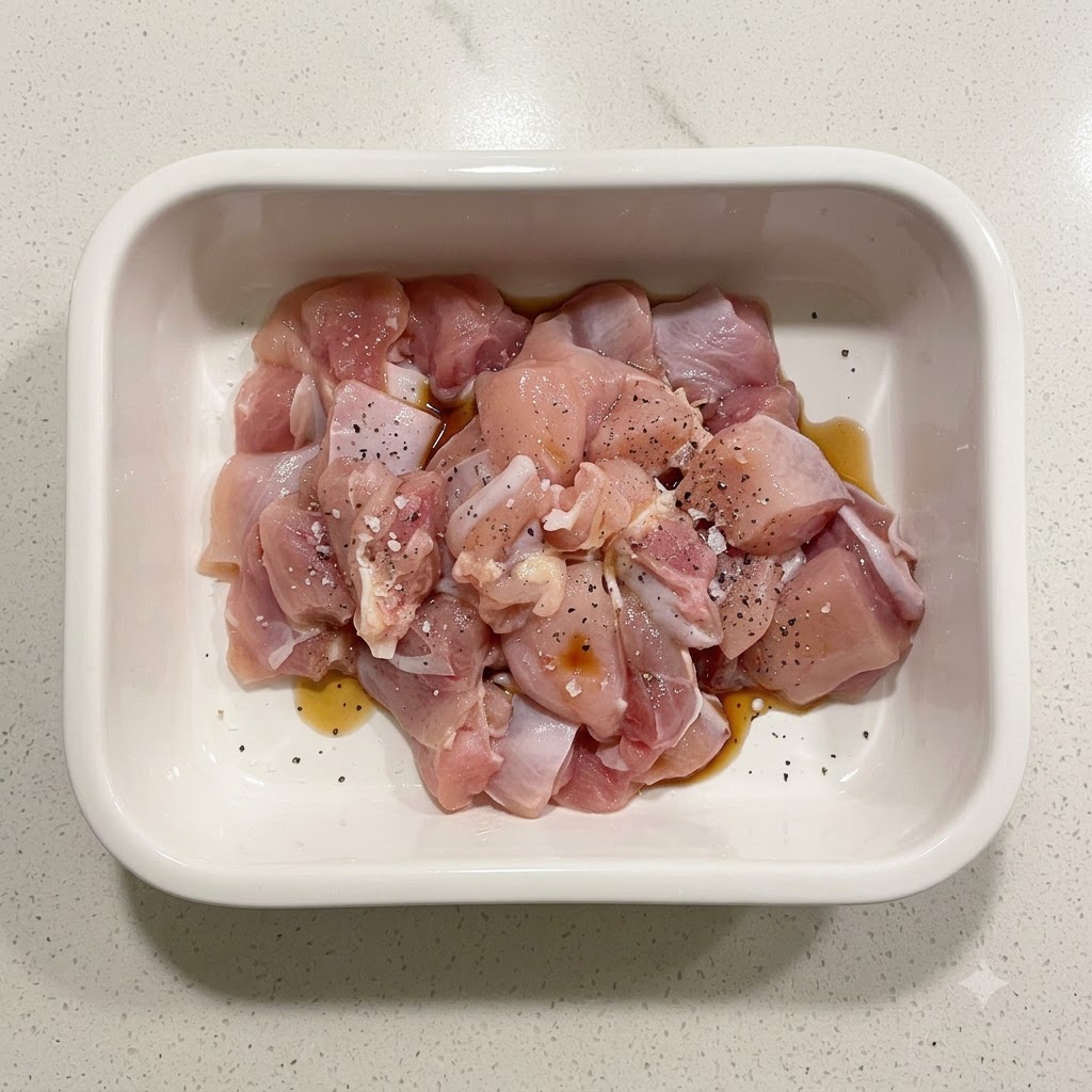 Morceaux de poulet cru assaisonnés avec de la fécule, de la sauce soja et du poivre noir dans un récipient en céramique blanche.