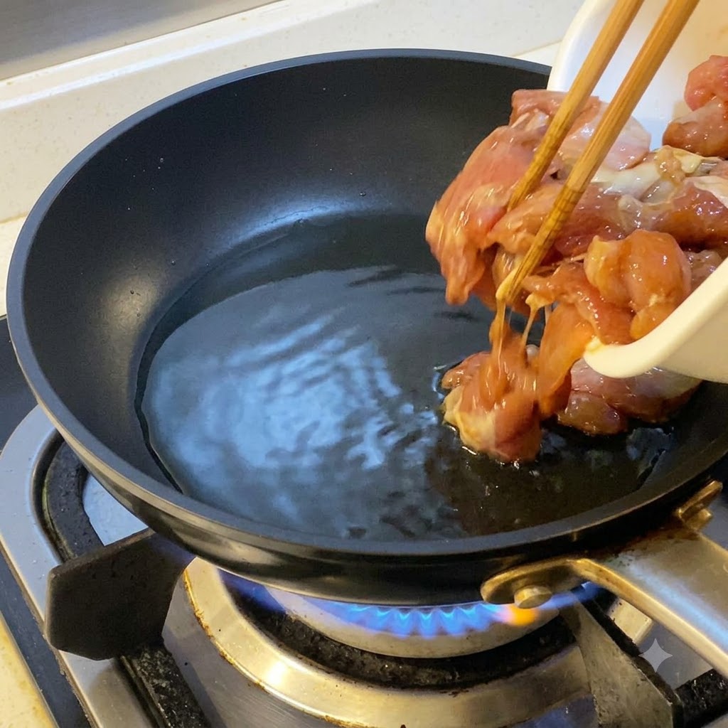 Morceaux de poulet marinés ajoutés avec des baguettes dans une poêle chaude huilée.