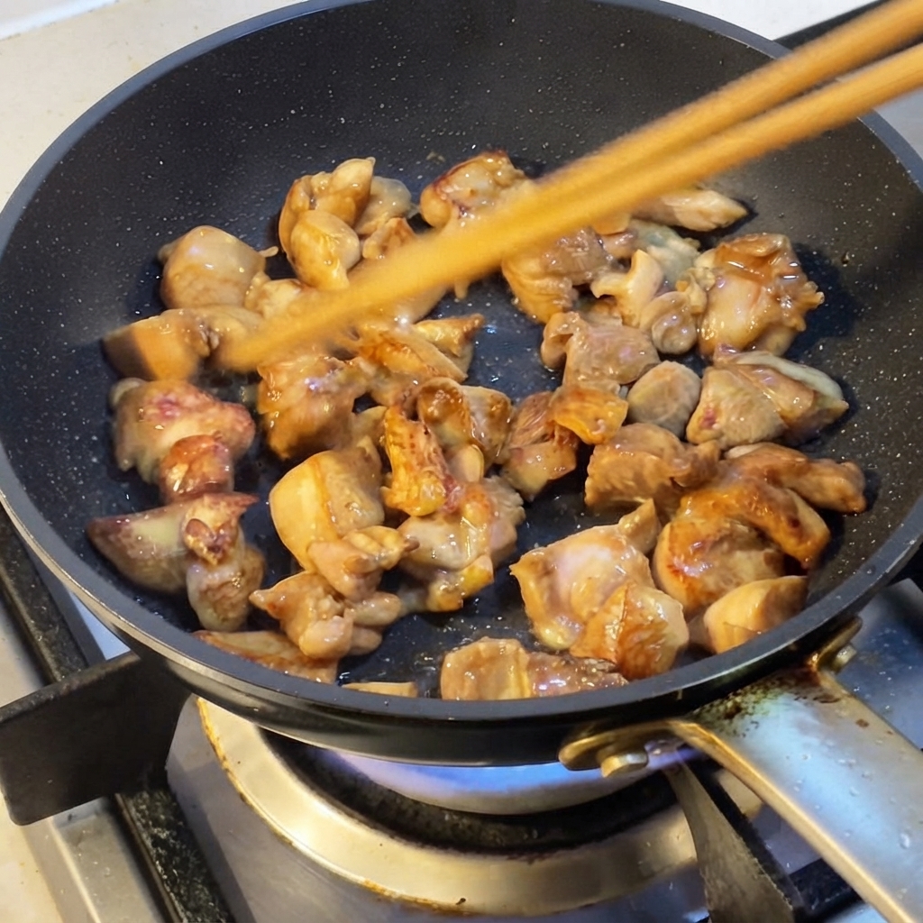 Morceaux de poulet sautés dans une poêle avec des baguettes.