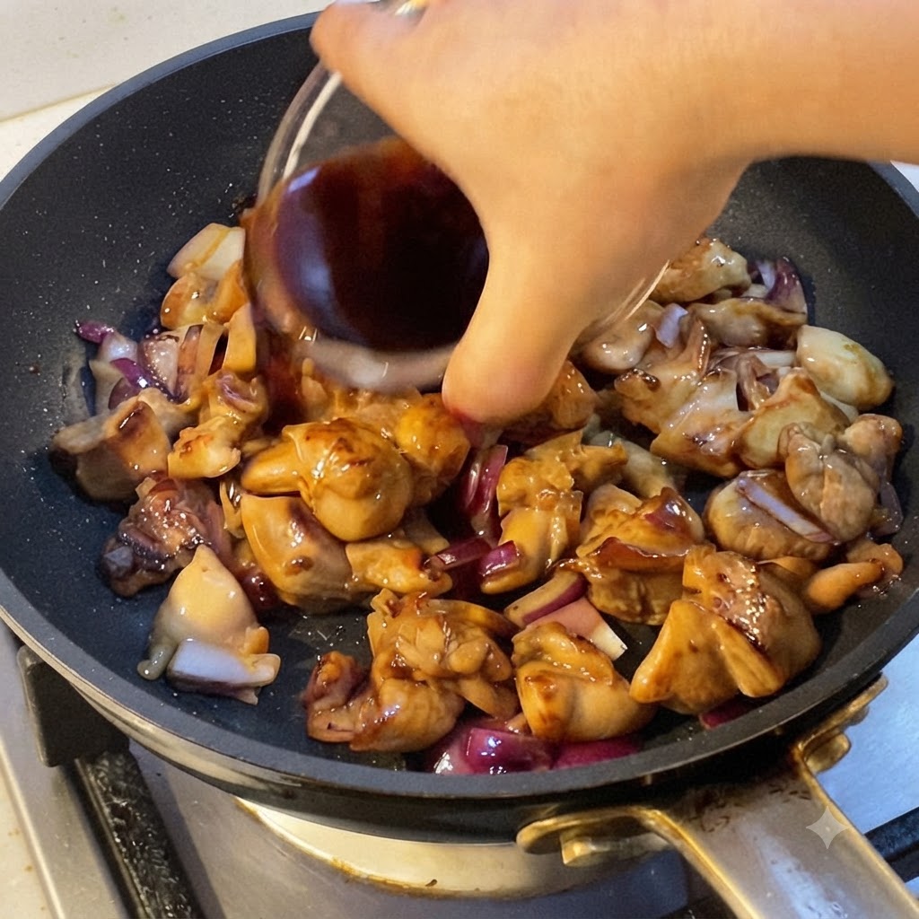 Une main versant une sauce de cuisson foncée dans une poêle remplie de morceaux de poulet cuits et doignon rouge.