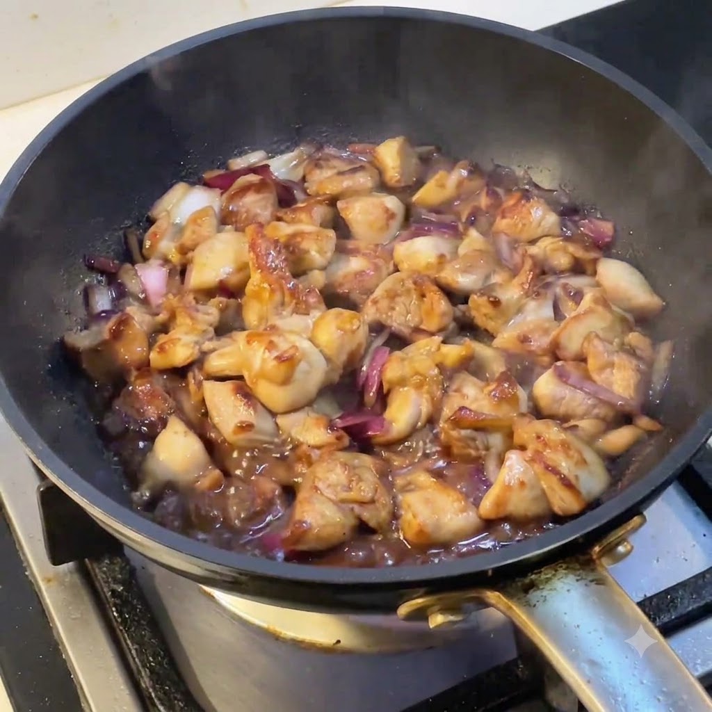 Une poêle remplie de poulet et doignons mijotant alors que de la vapeur sélève de la surface.