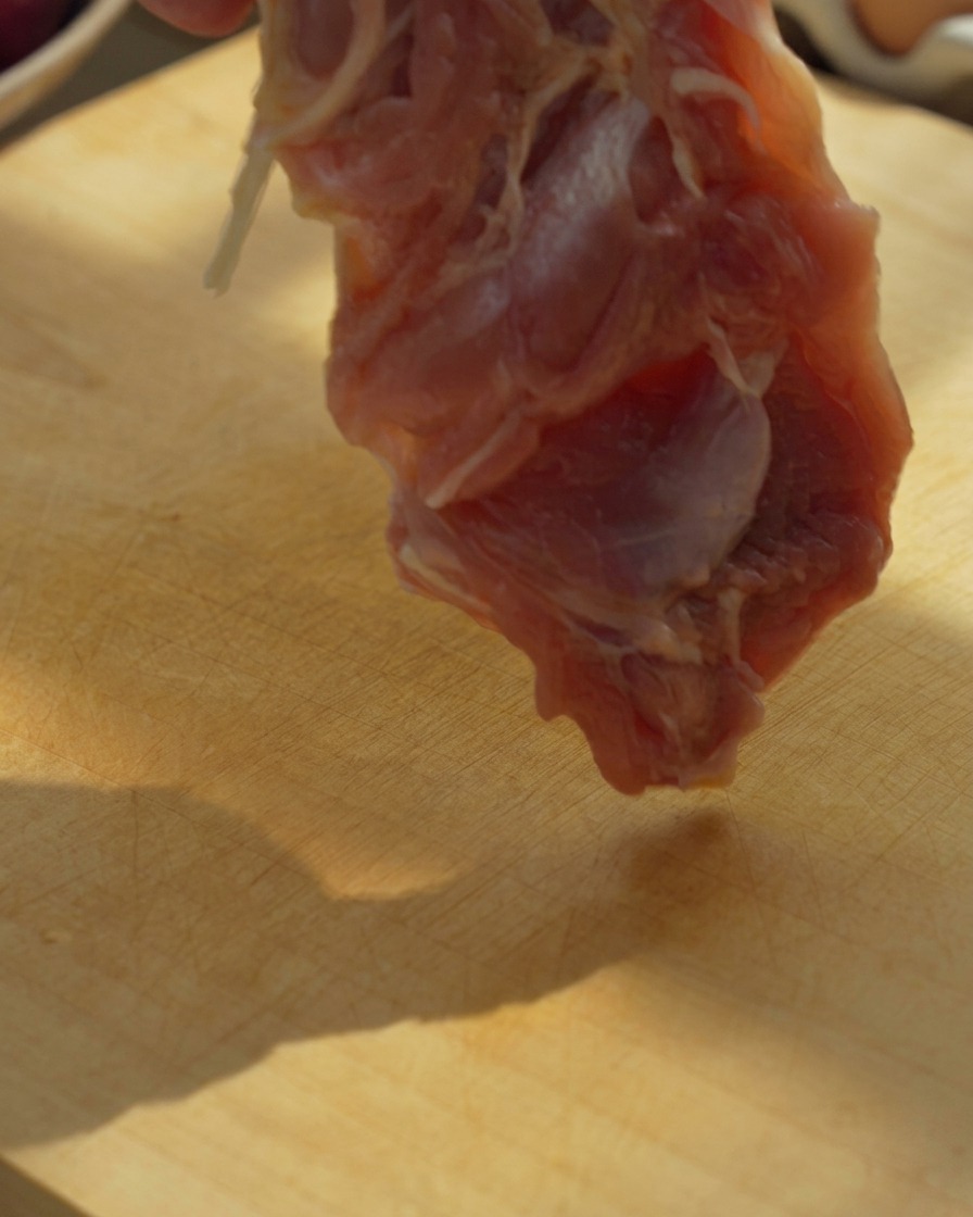 Filets de cuisse de poulet désossés coupés en gros morceaux sur une planche à découper en bois avec un couteau.