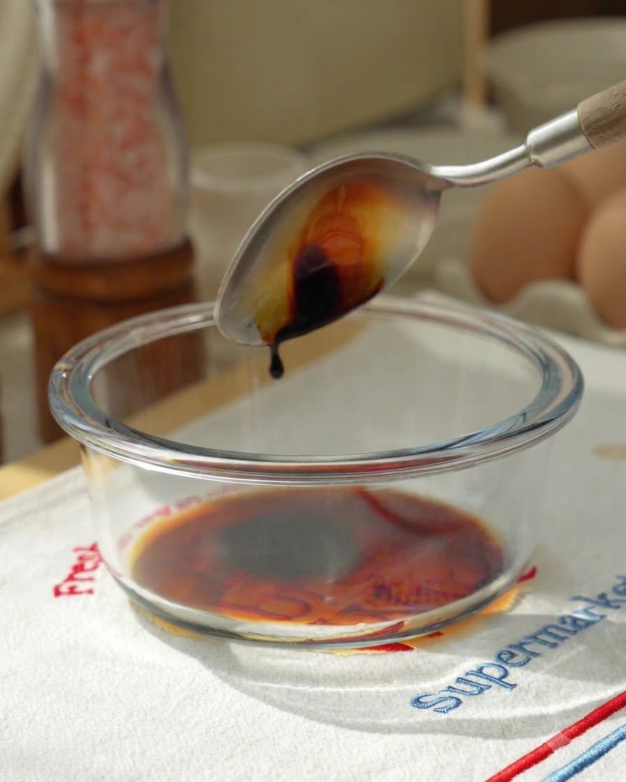 Sauce soja versée dune cuillère dans un bol mélangeur en verre contenant les ingrédients de la sauce.