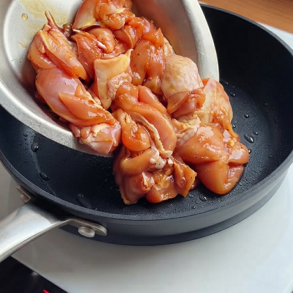 Des morceaux de poulet marinés versés dun bol dans une poêle noire bien chaude.