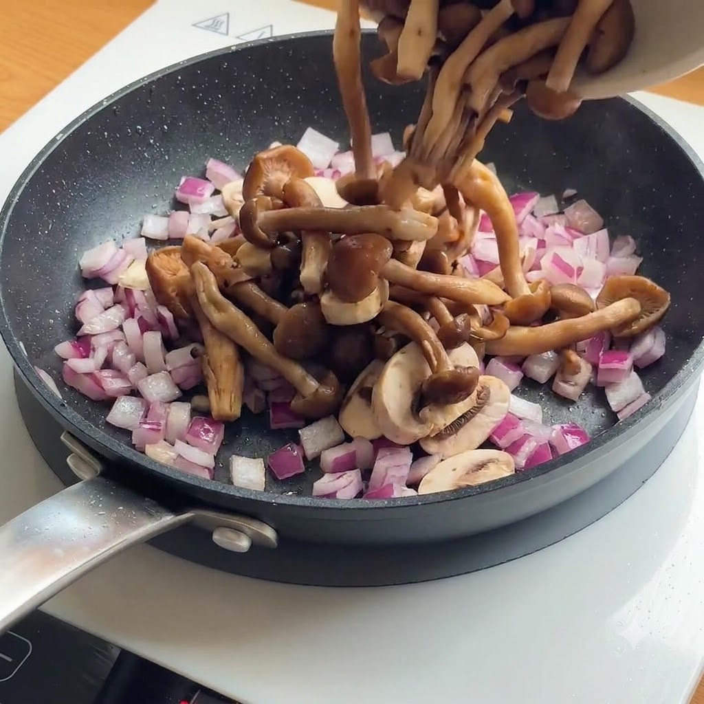 Des champignons tranchés et des oignons rouges ajoutés dans une poêle contenant déjà des morceaux de poulet dorés.