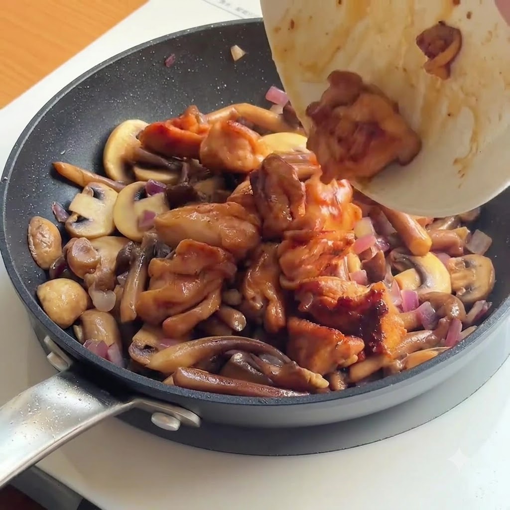 Du poulet cuit et du riz blanc versés dans une poêle remplie de champignons et doignons sautés.