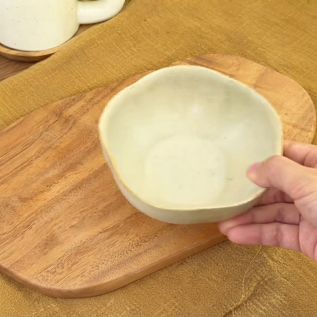 Un petit bol en céramique vide tenu au-dessus dune planche en bois prêt pour le mélange de la sauce.