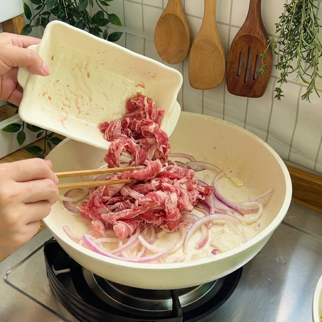 Des tranches de bœuf cru ajoutées dans la poêle avec les oignons pour le sautage.