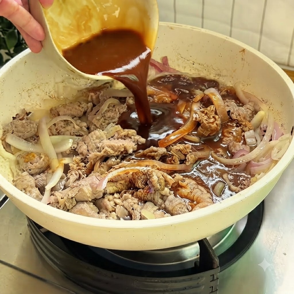 Une riche sauce brune versée dun petit bol dans une poêle blanche contenant le bœuf et les oignons tranchés.