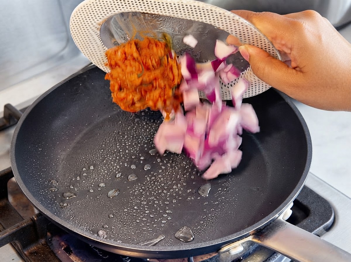 Oignons rouges en dés et kimchi rouge versés dune assiette passoire dans une poêle chaude avec des gouttes dhuile.