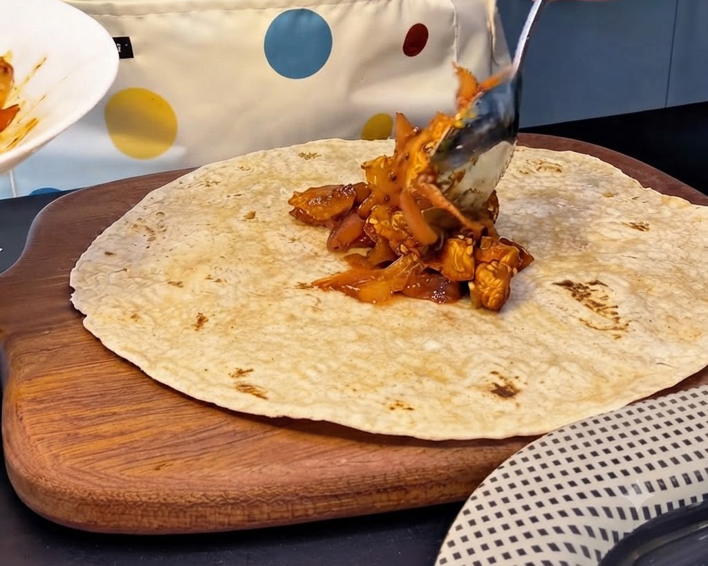 Une grande cuillerée de farce épicée au poulet et au kimchi placée au centre dune tortilla de blé complet.