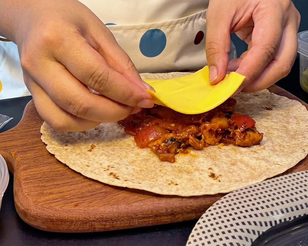 Mains plaçant une tranche de fromage jaune carré sur un tas de farce chaude au poulet et au kimchi sur une galette.