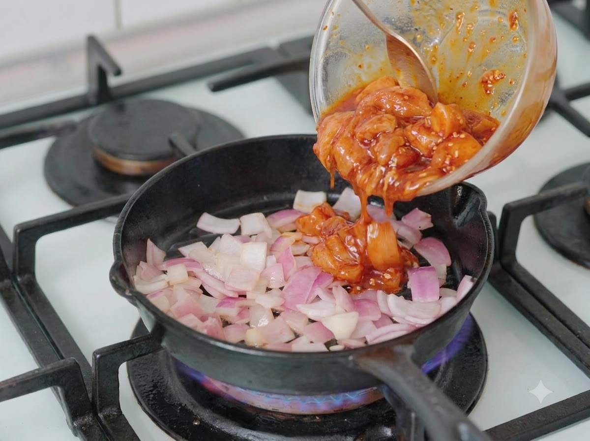 Morceaux de poulet marinés versés dun bol dans une poêle contenant des oignons émincés.