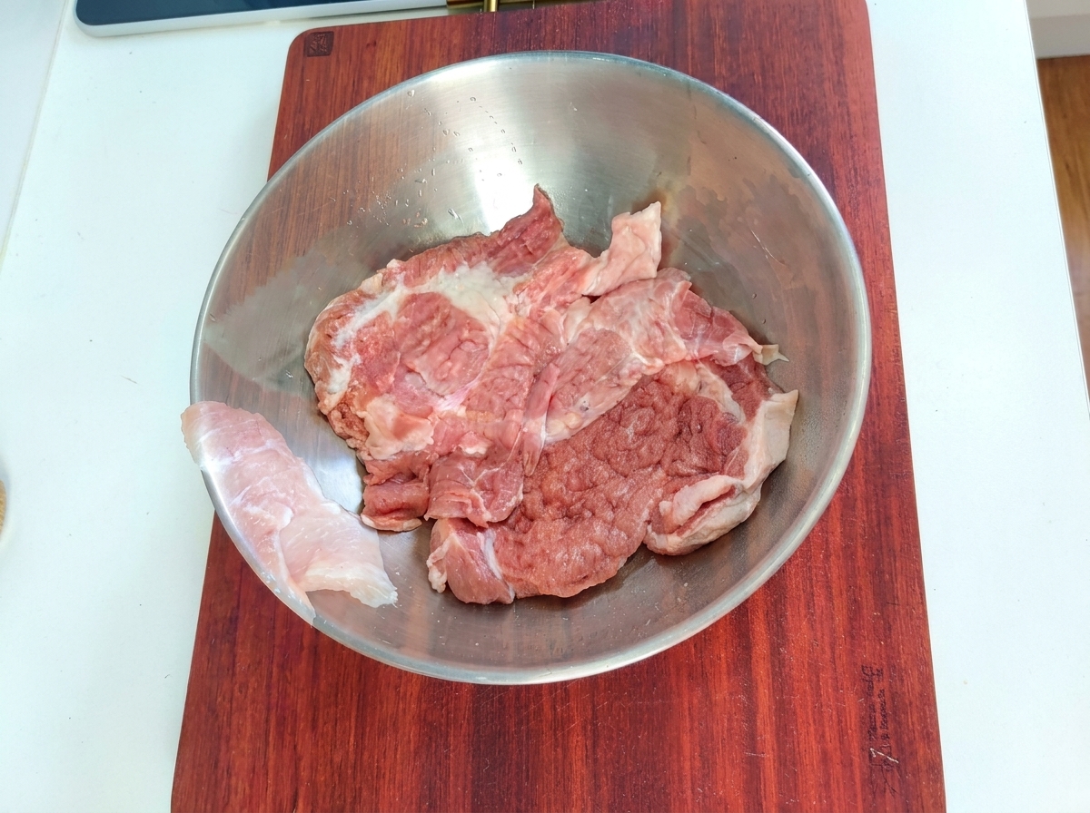 Morceaux de porc dans un bol mélangeur en métal avec les ingrédients de la marinade.