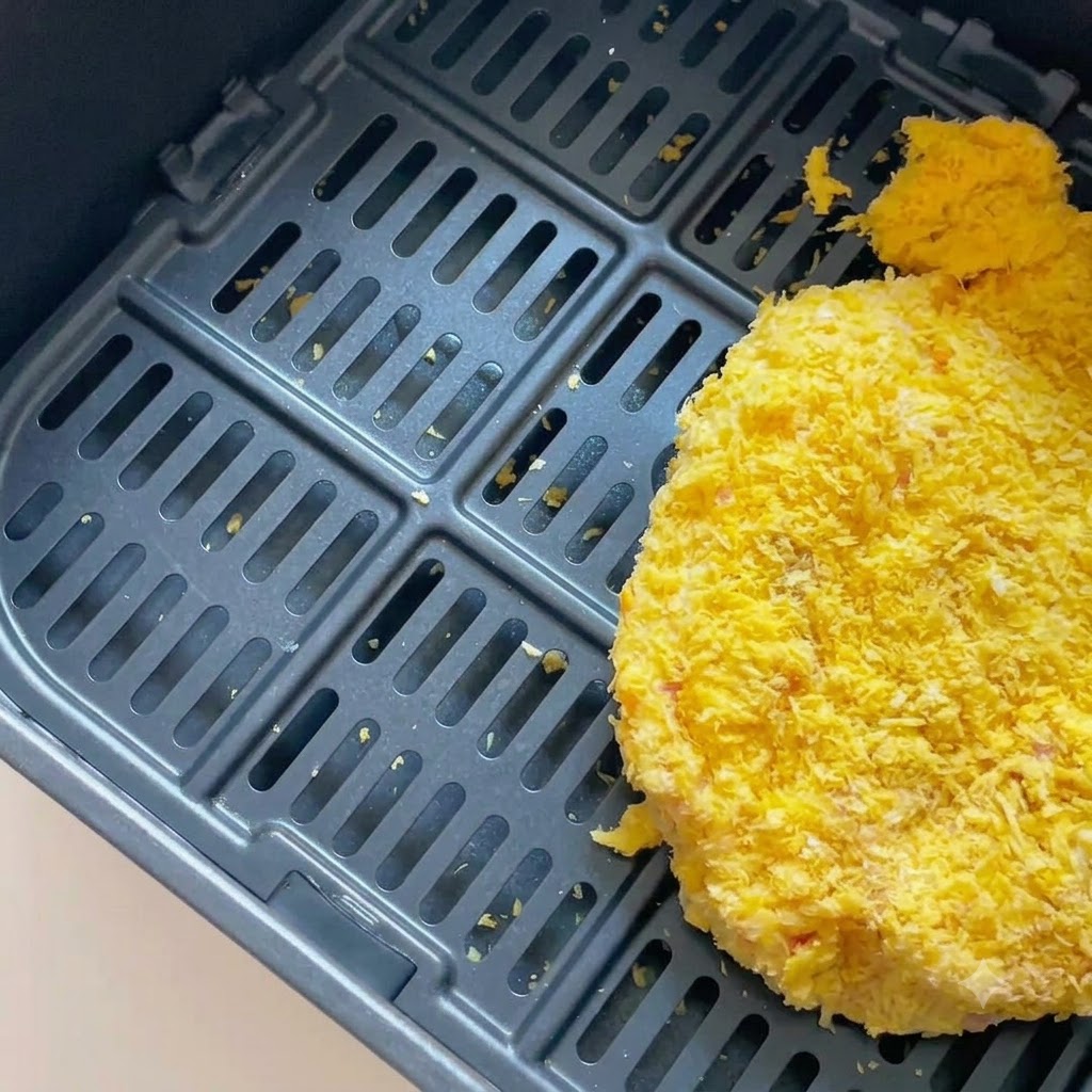 Une côtelette de porc panée disposée à lintérieur dun panier de friteuse sans huile noir.