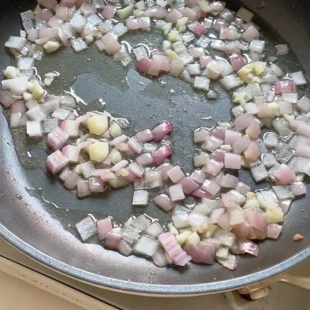 Pâte de curry ajoutée à la poêle contenant les oignons et lail sautés, en cours de mélange.