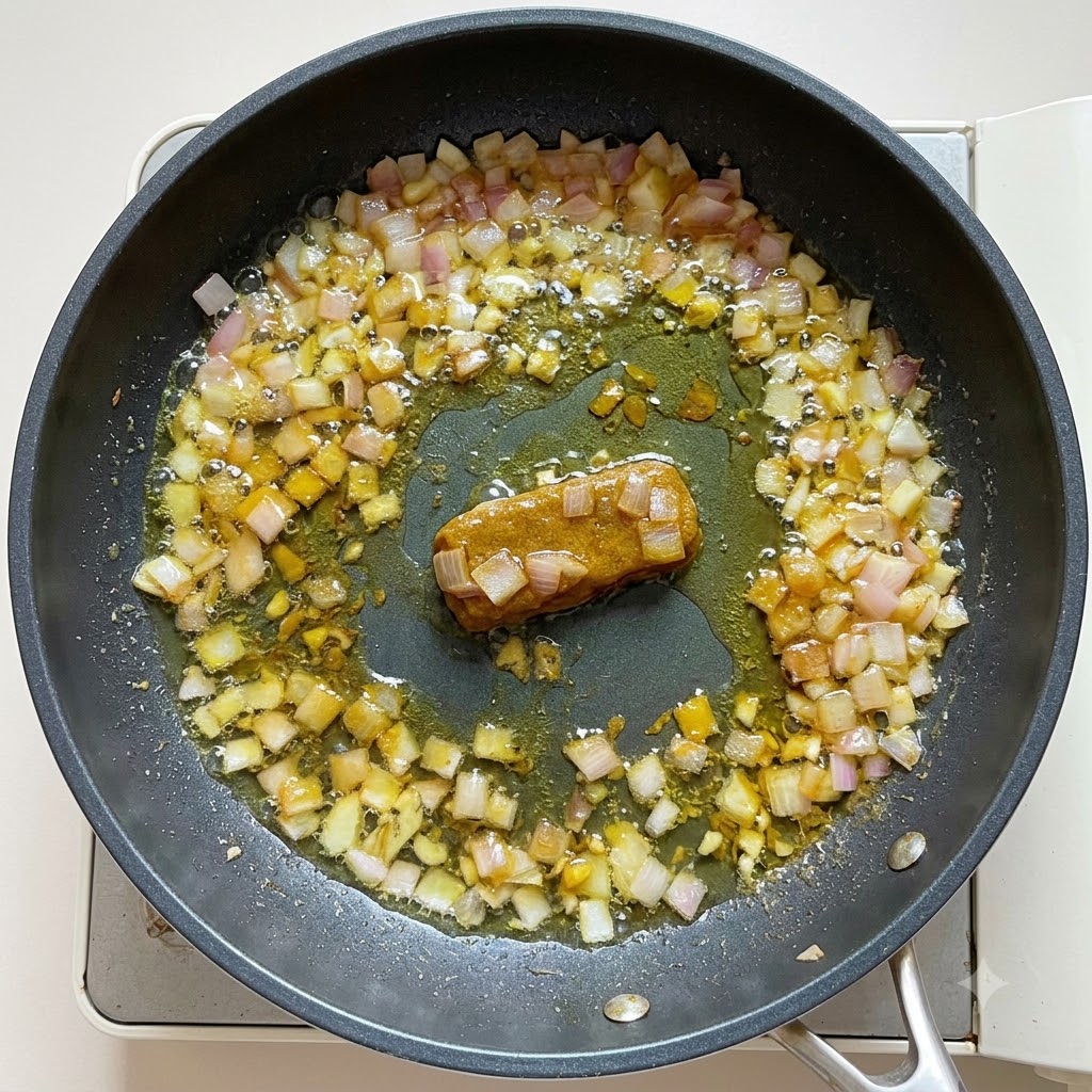 Eau et lait de coco versés dans la base de curry dans une poêle, remués pour obtenir une consistance épaisse.
