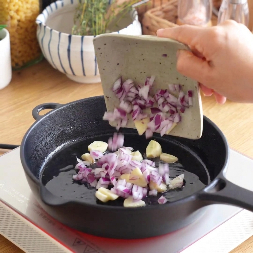 De loignon rouge haché et de lail tranché versés dun petit plat dans une poêle en fonte chaude.