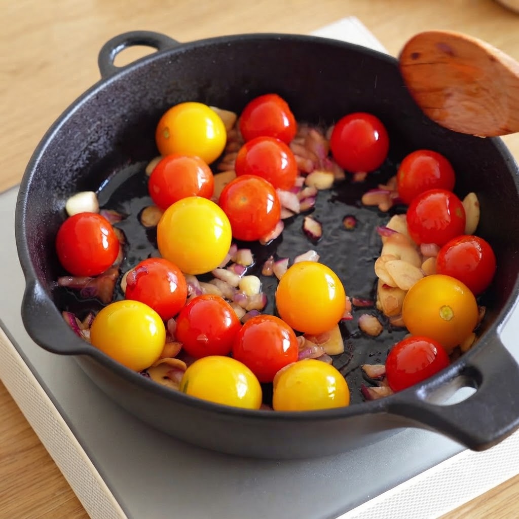 Une cuillère en bois tenue au-dessus dune poêle contenant des tomates cerises, des oignons hachés et de lail.