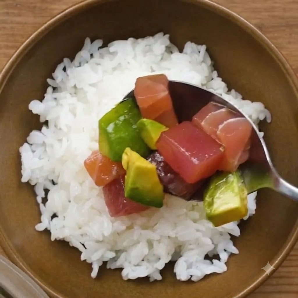 Une cuillère déposant le mélange mariné de thon et davocat sur un bol de riz blanc à sushi.